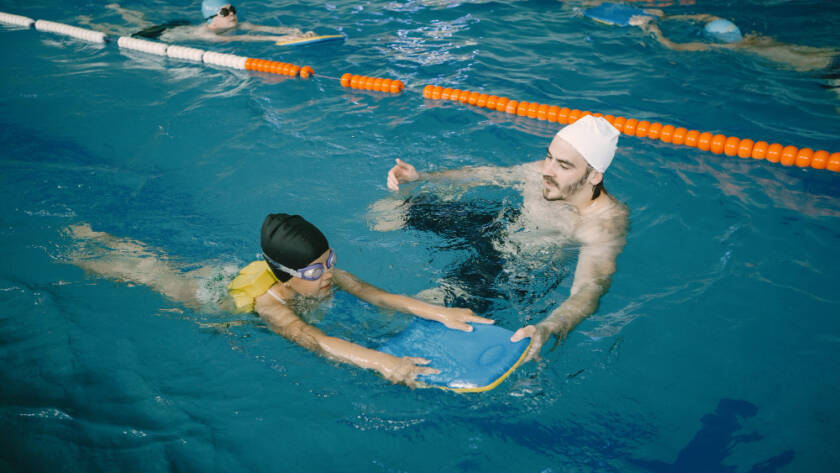 Coach teaching a child swimming technique in an indoor pool during swimming coaching for kids in Dubai lesson