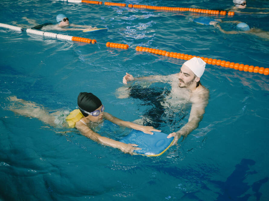 Coach teaching a child swimming technique in an indoor pool during swimming coaching for kids in Dubai lesson